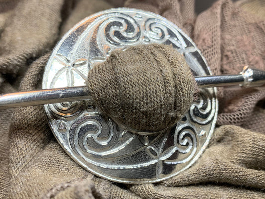 A decorative shawl pin fastening a knitted wrap