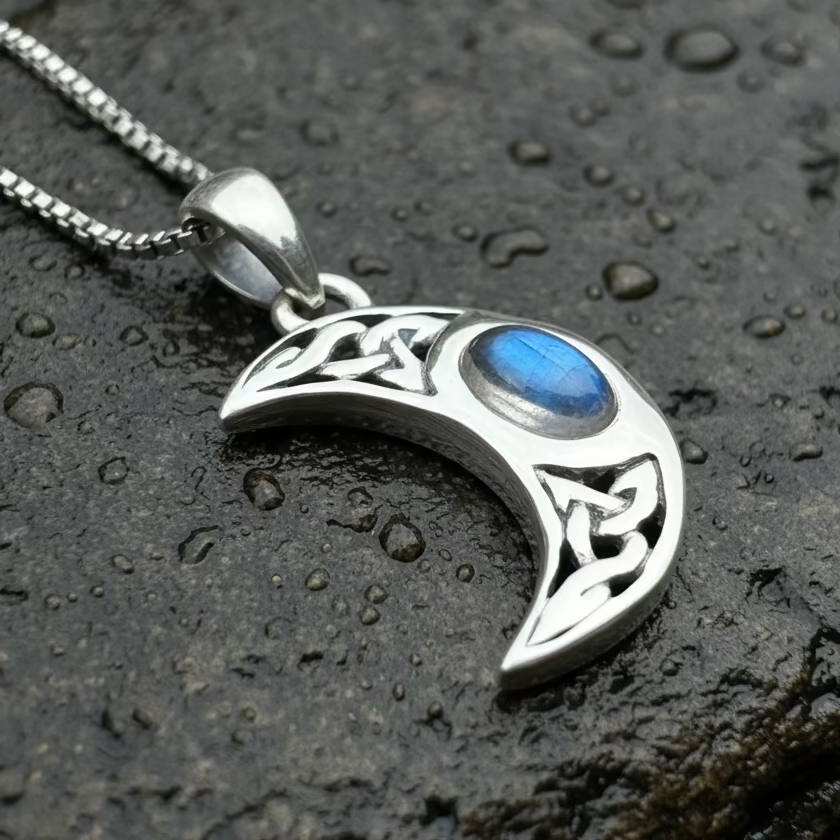 Silver crescent moon pendant with blue stone on a dark textured surface