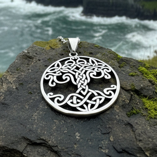 A silver Celtic knot tree of life pendant necklace resting on dark gray and light beige stones.