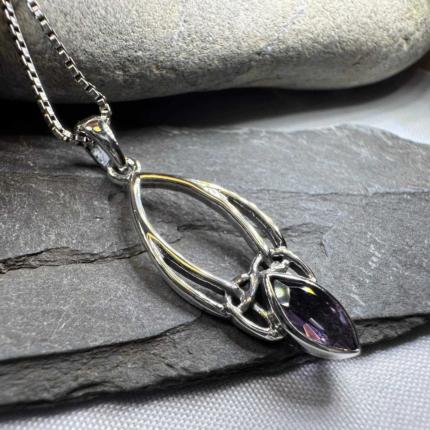 Silver necklace with a purple gemstone pendant on a stone surface