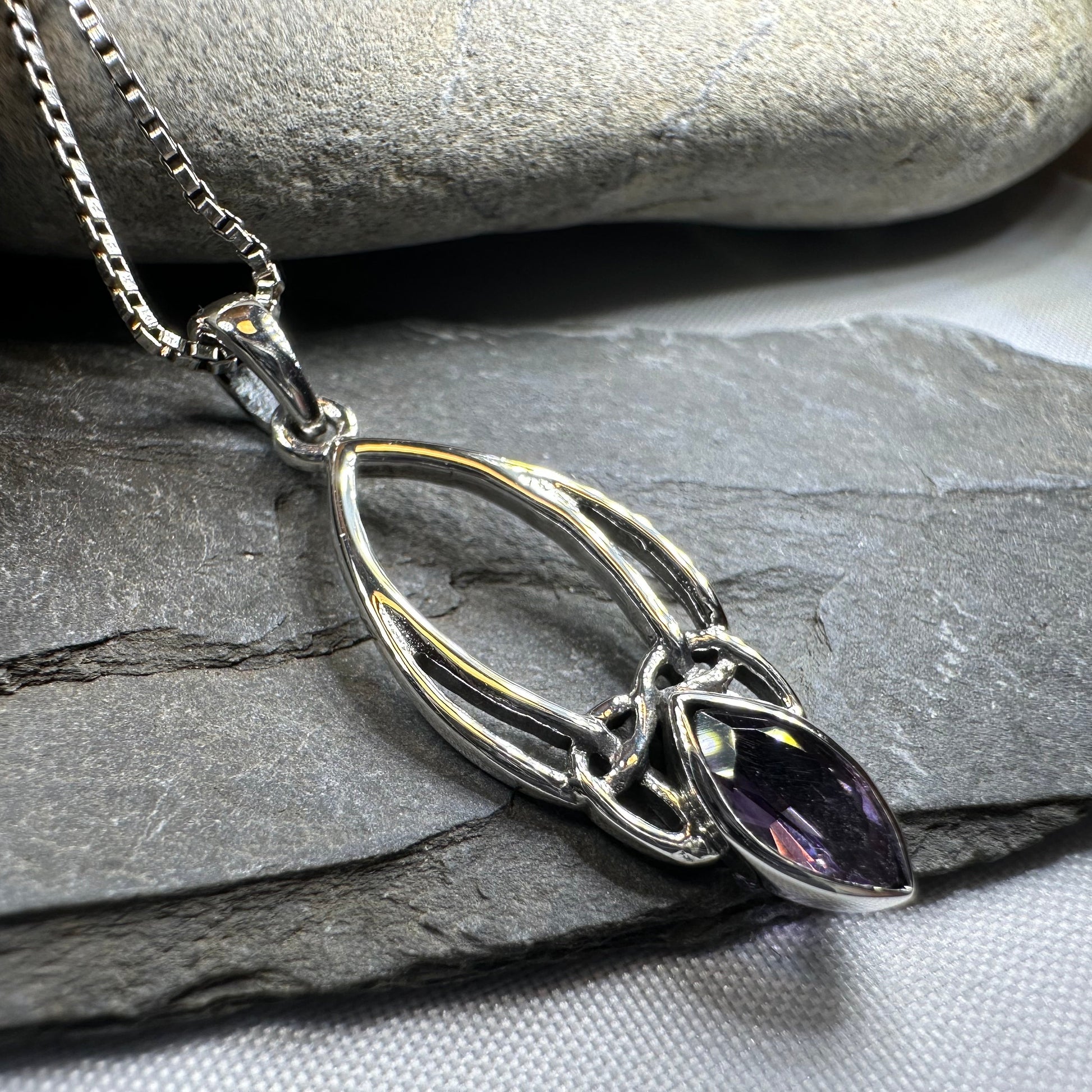 Silver necklace with a purple gemstone pendant on a stone surface