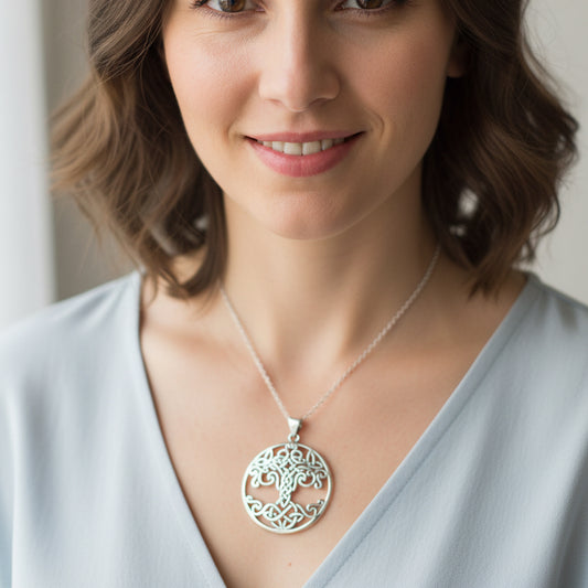 A silver Celtic knot tree of life pendant necklace resting on a smooth gray stone.