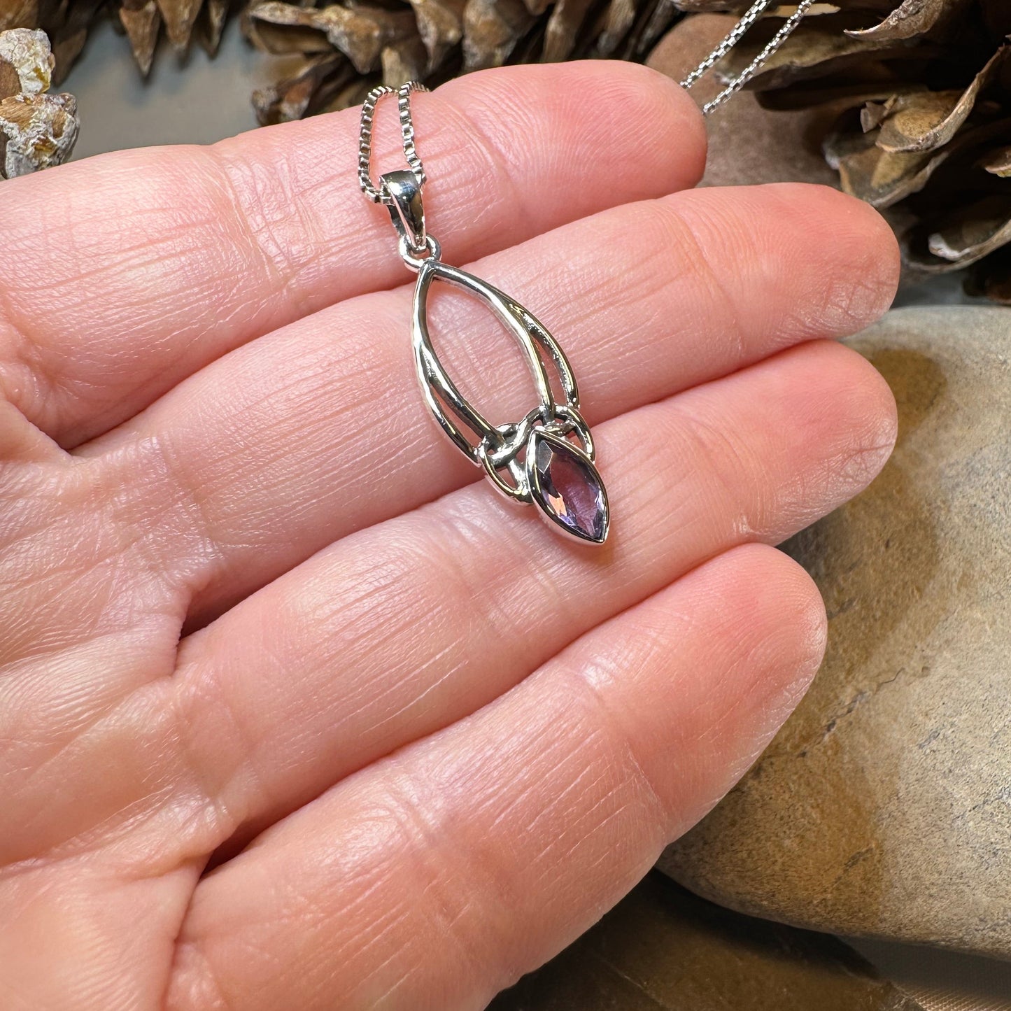 Hand wearing a silver ring with a gemstone, surrounded by natural elements.