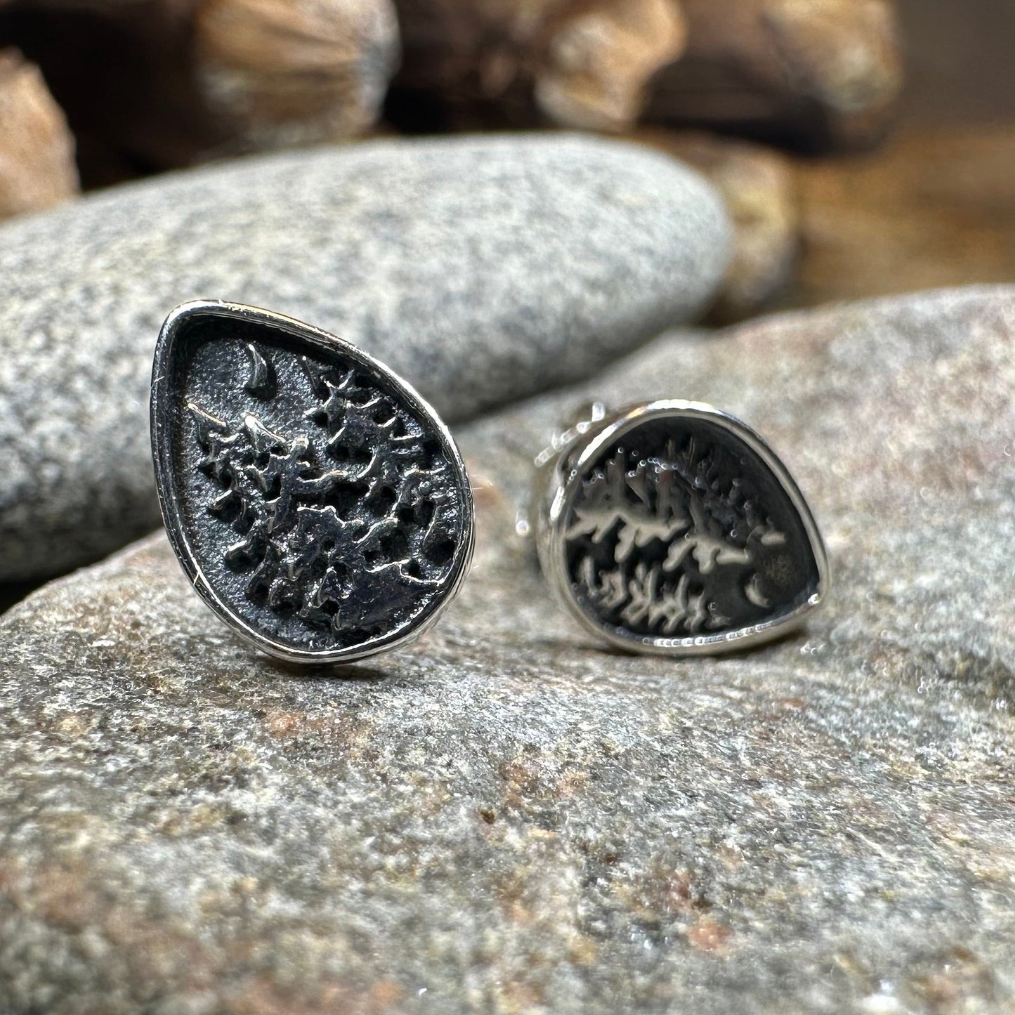 Silver teardrop-shaped earrings on a textured stone surface with a natural background.