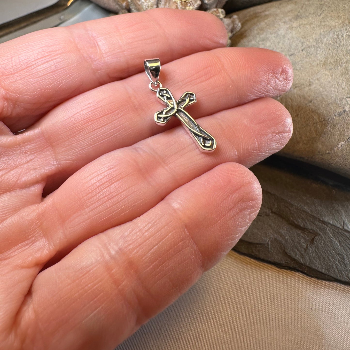 Silver cross pendant held between fingers with a natural stone background