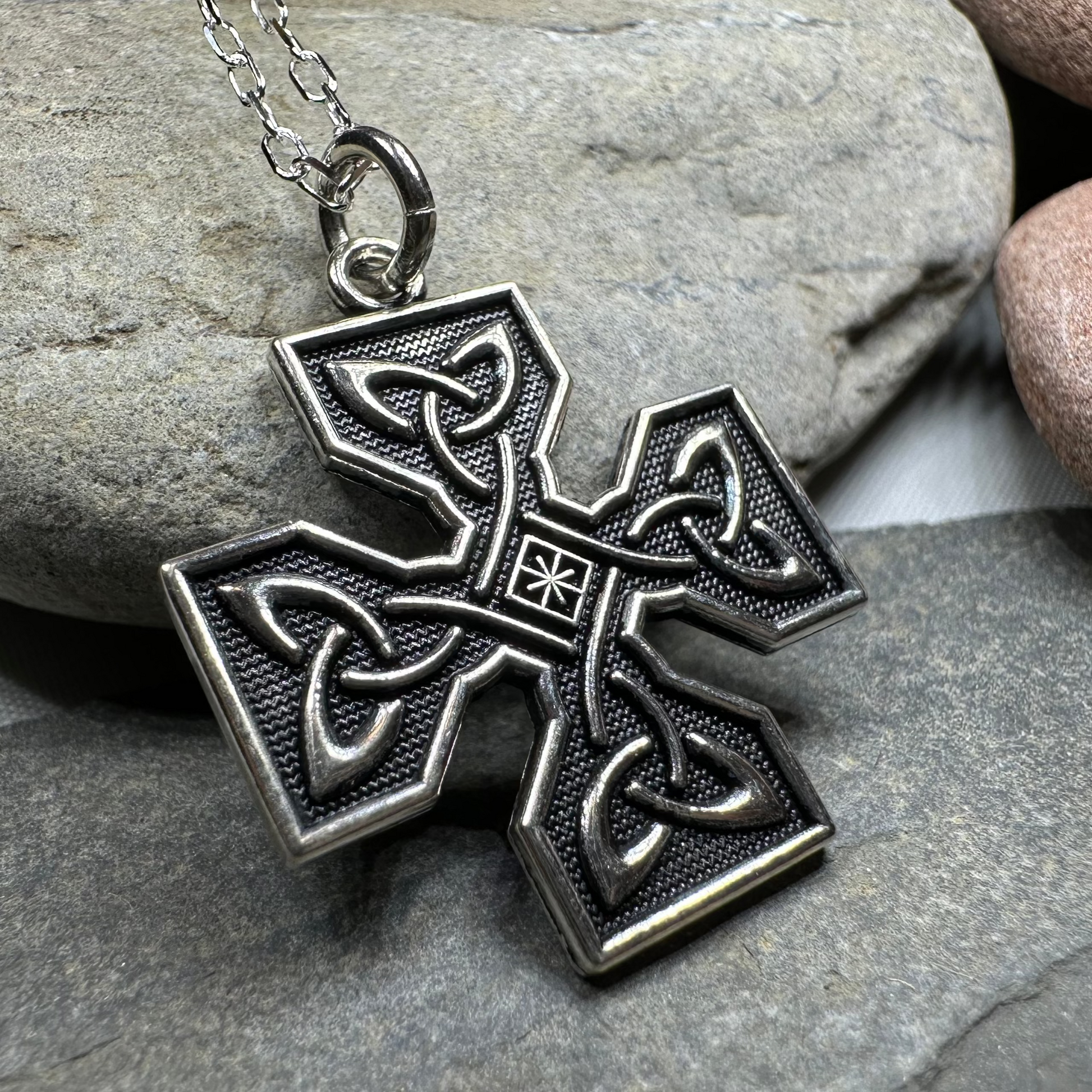 Silver cross pendant necklace on a stone surface