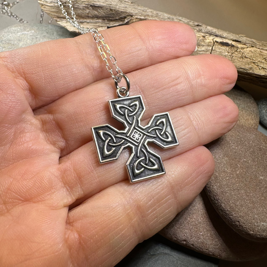 Silver cross pendant held in a hand with a natural background