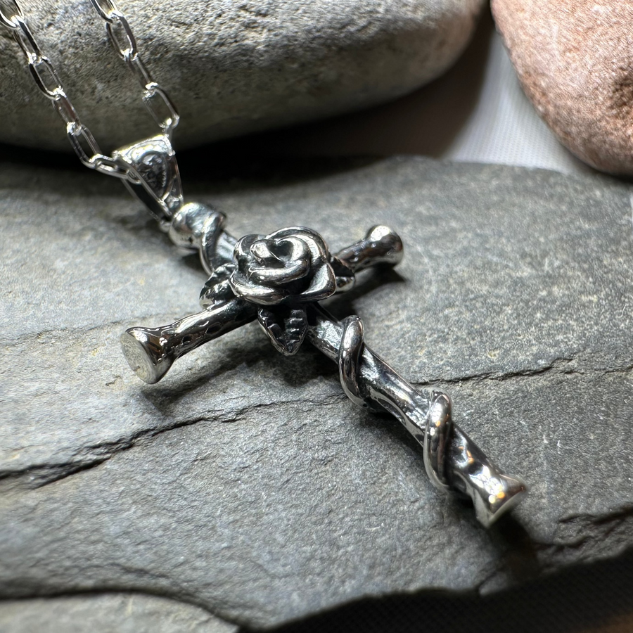 Silver cross necklace with rose detail on a stone surface