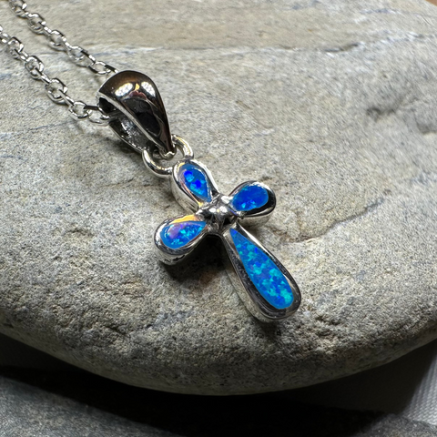 Load image into Gallery viewer, Blue opal cross pendant on a chain against a stone background
