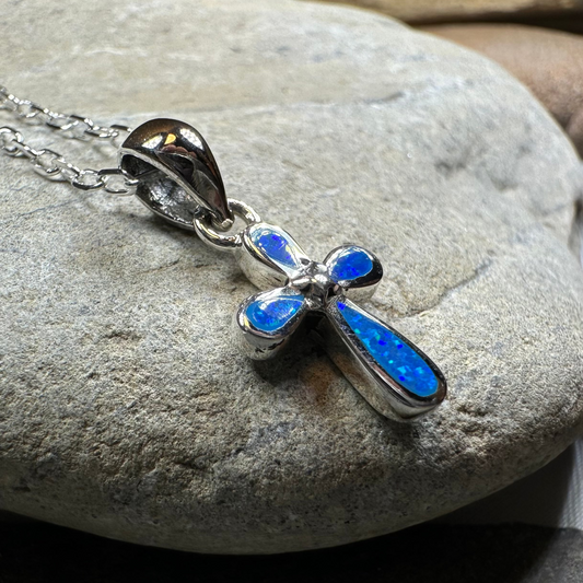 Blue opal cross pendant on a silver chain against a stone background
