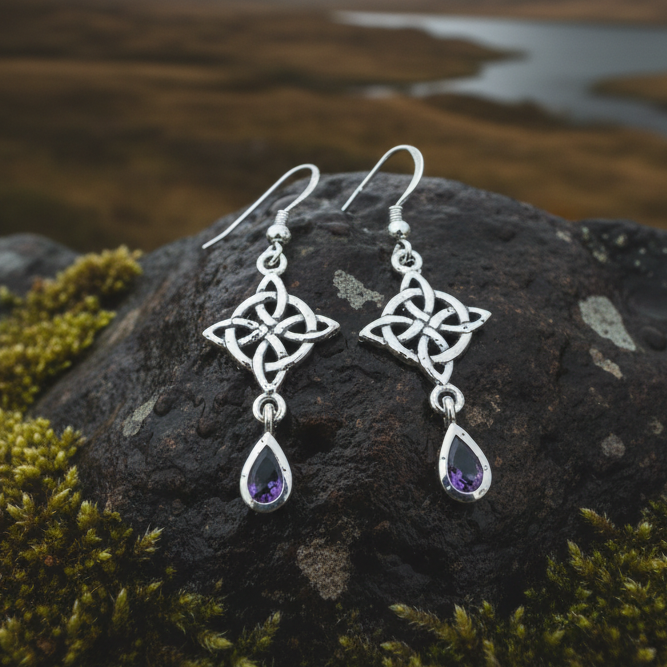 Silver earrings with purple gemstones on a wooden surface with purple flowers.